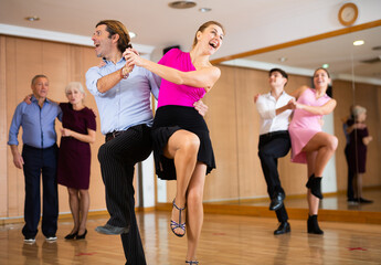 Cheerful adult amateur couple practicing vigorous lindy hop moves in dance class. Social dancing...