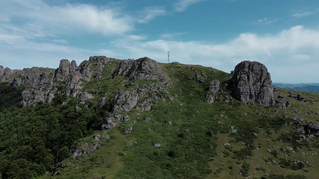 Rocky peaks of Babin Zub mountain in Stara Planina National Park, Serbia, rise above green forests under a blue sky. Aerial view from drone. Horizontal 4k footage