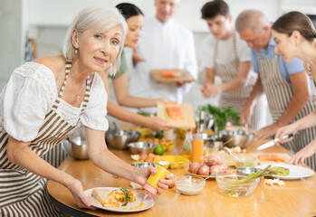 Elderly woman in apron pours sauce into ready dish at cooking master class