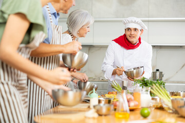 Positive young male instructor of culinary classes explaining his students how to make sauce for meal
