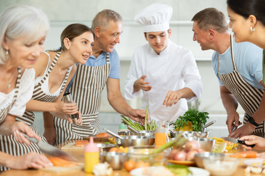 Friendly smiling young woman talking to culinary enthusiasts during group cooking masterclass from professional chef..