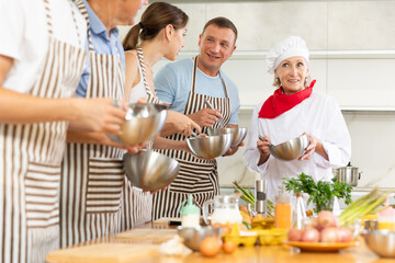 Adult students prepare food according to recipe in cooking class led by a female chef