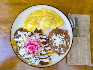 An omelet with chilaquiles topped with sauce, cream, cheese, and pickled onions, served with refried beans topped with cheese