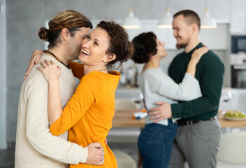Two married couples dance during holiday, have fun, move and jump in dining room. Family event is held with fun music and dancing