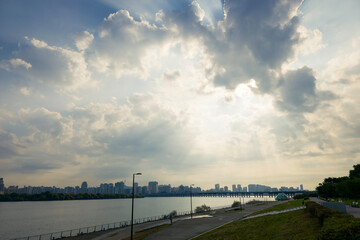 Sunlight streaming through clouds above river and skyline