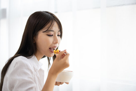 Young Woman Eating Cereal by the Window in Morning Light