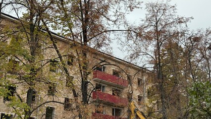 Obraz premium Old brick residential building with red balconies and autumn trees. Concept of urban decay, renovation and city transformation 