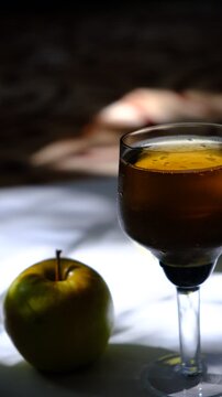 Glass of brut apple cider from Normandy. White table with casting shadows and sunlight. Ripe yellow fruits on the table. Atmospheric mood.
