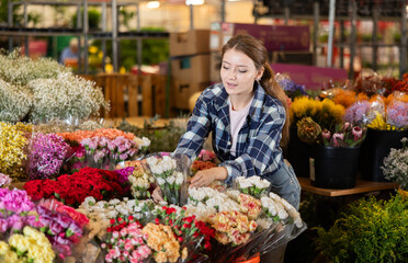 Girl salesman takes out bunch of carnation from showcase, creates bouquets, combines flowers and decorative herbs. Supply and demand, assortment of flowers for ceremonial and ritual bouquets.