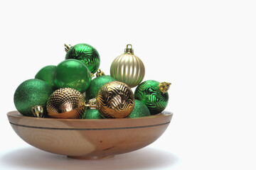 A hand crafted wooden bowl with green and gold Christmas ornaments on a white background. The...