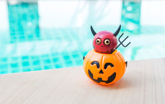 Red devil on Halloween pumpkin lantern with space on swimming pool background, outdoor day light, Happy halloween background idea