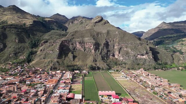 Pisac, Peru: Aerial drone footage with upward motion showing the Pisac town, located in Peru's sacred valley region surrounded by mountains and ancient Inca ruins. 