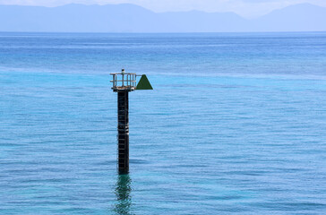 Navigation marker with a green triangle in a blue ocean with mountains in the background