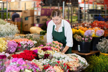 Female employee uses carnation flowers to create bouquet. Flower megamarket, potted and cut flowers, gardening ideas, gardening supplies.