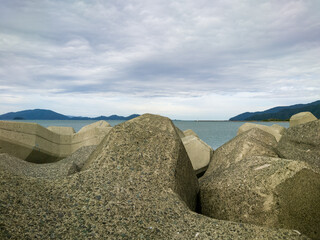 テトラポットとも呼ばれる消波ブロックが設置されている海沿いの防波堤のイメージ