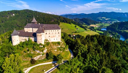 Panoramic view of a medieval castle perched on a hillside, surrounded by lush forests, rolling hills, and a river valley