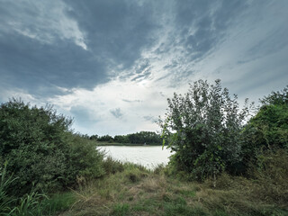 Wide view of Jezero Borkovac near Ruma, Serbia, framed by shrubs and trees under a dramatic...