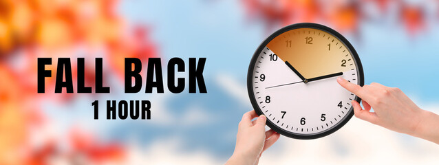 Hand adjusting clock to fall back one hour in autumn