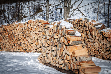 Stacks of split firewood in the snow, Slovenia. Neatly piled logs dry and season outdoors, showing grain, bark, and fresh cut surfaces. A classic rural winter scene linked to heating and biomass fuel.