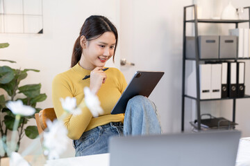Smiling young Asian woman, a creative professional or entrepreneur, working on a digital tablet with a stylus in a casual modern office