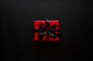 Black Friday background with a single luxurious red gift with black ribbon on dark background ideal for sales.