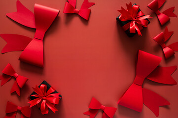 Black Friday concept with red ribbons, bows, and two small black gifts frame a vibrant red background for holiday sales copy.