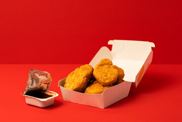 Chicken nuggets in a paper container and dark brown dipping sauce.  紙容器に入ったチキンナゲットとこげ茶色のソース（バーベキューソースなど）