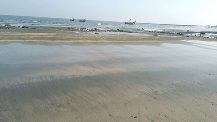 Sandy beach with calm ocean and fishing boats in the distance water