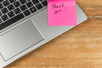 Note on laptop expressing gratitude placed on wooden desk