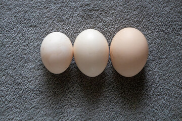 Three chicken eggs on gray textured surface.