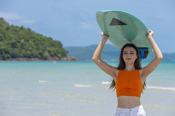 Confident young woman holding surfboard over head on tropical beach, wearing orange crop top and white shorts. Great for themes of summer adventure, surfing lifestyle, and beach vacation freedom.