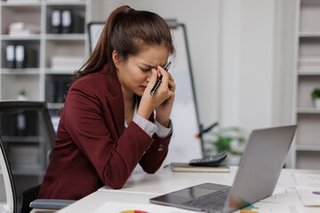 Tired business woman in stress works at a laptop while sitting at a table at office and holds her hand on her temples, migraine attack. Freelance, work from online. 
