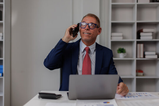 Happy smiling laughing American positive ethnic man business employer entrepreneur smile pleasant conversation smartphone call talk mobile phone businessman guy male in office typing laptop