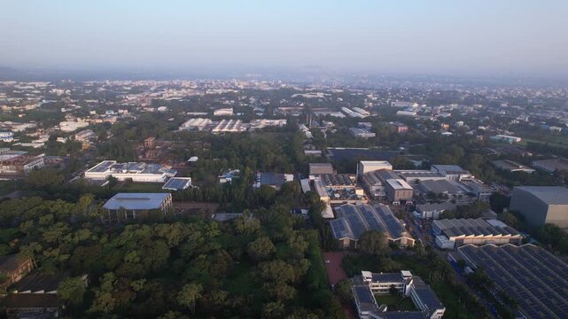 Tier 2 nashik city industrial buildings with rooftop solar panels surrounded by green parks covered in morning haze, Maharashtra, Aerial