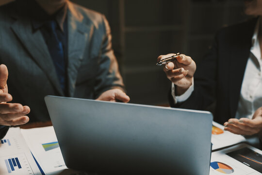 Business colleagues collaborating on strategy, analyzing financial data with graphs and charts, using a laptop in a corporate office setting - Powered by Adobe