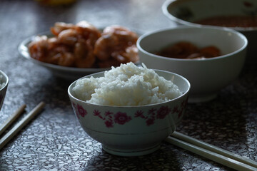A traditional Vietnamese family meal with a bowl of white steamed rice in the foreground and cooked shrimp dishes in the background
