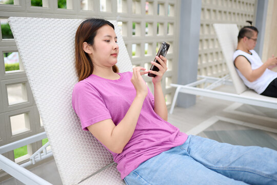 A young woman relaxing on a lounge chair, engrossed in her smartphone - Powered by Adobe