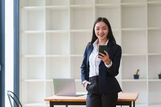 Young Asian businesswoman smiling, connecting and receiving good news on her smartphone in a modern office environment