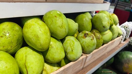 Fresh green mangoes neatly stacked on wooden crates at a market. The image captures the vibrant color and texture of tropical fruit, symbolizing freshness, healthy food, and organic produce.