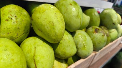 Fresh green mangoes neatly stacked on wooden crates at a market. The image captures the vibrant color and texture of tropical fruit, symbolizing freshness, healthy food, and organic produce.