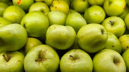 Fresh green apples piled together at a market display. The vibrant color and natural texture...