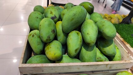 Fresh green mangoes neatly stacked on wooden crates at a market. The image captures the vibrant color and texture of tropical fruit, symbolizing freshness, healthy food, and organic produce.
