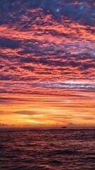 A breathtaking ocean sunset with vivid orange, pink, and purple clouds reflecting on gentle waves. A lone sailboat drifts on the horizon, capturing the serene and dramatic beauty of twilight at sea.