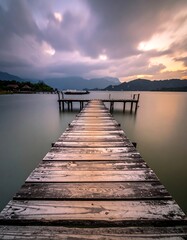 Naklejka premium Wooden pier extending into calm water with dramatic cloudy sunset