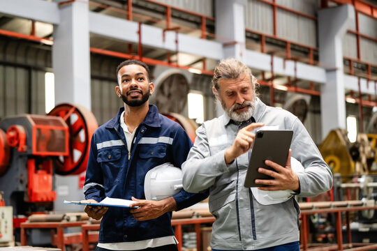 Senior factory manager guiding a young worker during an inspection. Analyzing production data on a tablet. Teamwork and leadership in an industrial business. Making an inspection together with team.