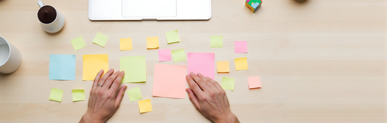 Hands organizing colorful sticky notes on desk with laptop  