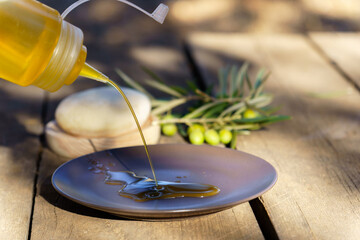 Pouring fresh extra virgin olive oil from a squirt bottle onto a plate, with olive branches in the background