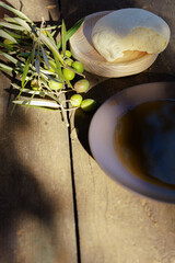 Freshly picked olive branches, extra virgin olive oil, and rustic bread on a wooden table, capturing a mediterranean food concept