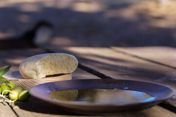 Extra virgin olive oil in a bowl, bread, and green olives on a rustic wooden table capturing mediterranean cuisine