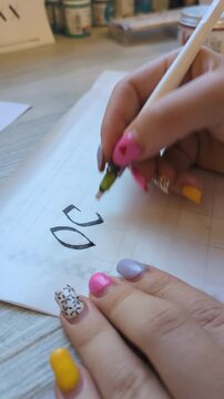 Artistic calligraphy in progress, hand holding pen creating elegant script on paper. Concept of handwriting practice, craftsmanship, and personal artistic style.